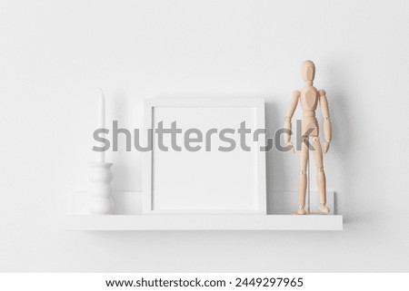 White square frame mockup with manikin and candle decoration on the wall shelf.