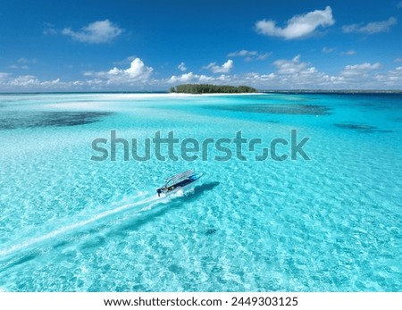 Aerial view of floating boat in transparent azure water on sunny summer day. Mnemba island, Zanzibar. Top view of yacht, sandbank in low tide, clear blue sea, sand, sky with clouds. Motorboat in ocean Royalty-Free Stock Photo #2449303125