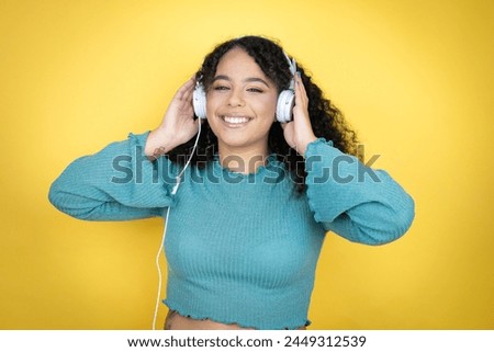 African american woman wearing casual sweater over yellow background using headphones dancing and listening to music with a happy face standing and smiling with a confident smile showing teeth