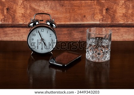 Alarm clock with glass of water and mobile phone on a wooden bedside shelf