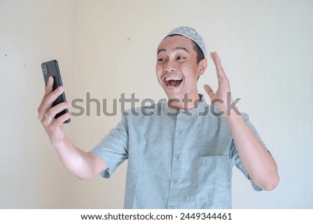 Moslem Asian man happy during video call with smartphone when Ramadan celebration. The photo is suitable to use for Ramadhan poster and Muslim content media.