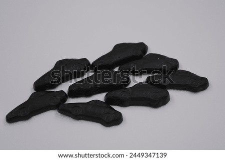 Unusual and non-standard jelly candies in the form of very black cars, cars located on a white plastic background. Royalty-Free Stock Photo #2449347139