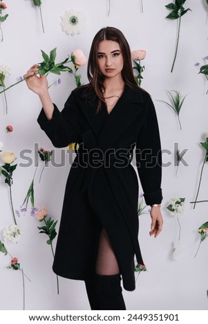 Vertical photo of young woman poses near flowers hanging in air on white background. Photo studio location for photoshoot