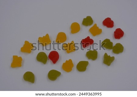 Unusual and non-standard, small jelly candies in the form of yellow, red, green butterflies, shells, flowers located on a white plastic background. Royalty-Free Stock Photo #2449363995