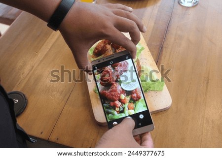 man hand is using a mobile phone to take a picture of food on the dining table in the restaurant. Photography with Mobile Phone Concepts.Taking photo by cellphone before eating