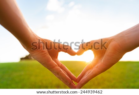 Love shape hands against natural sunset background