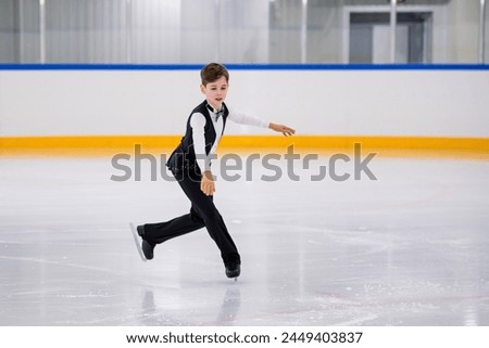 A young boy is skating on ice with his arms outstretched. He is wearing a black outfit and he is performing a trick