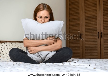 Lonely woman sits on the bed in bedroom and hugging pillow. Depressed woman with blank expression. Royalty-Free Stock Photo #2449409115