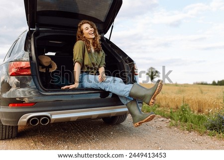 Young woman enjoying fresh air sitting in open trunk. Journey by car. Lifestyle, travel, tourism, nature concept. Royalty-Free Stock Photo #2449413453