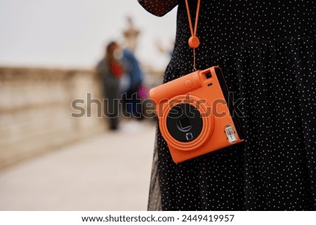 Woman holding orange instant camera. Tourist captures memories during travel with vintage camera
