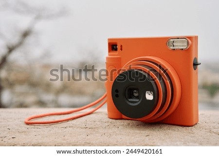 Vintage Orange Instant Camera in city with cloudy sky. Travel shooting equipment
