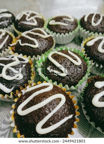 A picture of a bundle of home-baked chocolate cupcakes decorated by white chocolate frosting, made in colorful cupcake liners.