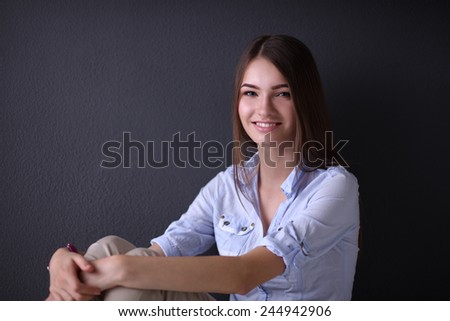 Portrait of young woman sitting on the floor near dark wall