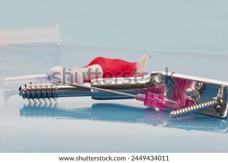 Hip fracture surgery concept. Dynamic hip screw for fixation of hip fracture, percutaneous entry needle, peripheral intravenous catheter on light blue background Royalty-Free Stock Photo #2449434011