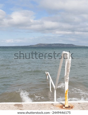 Submerged handrails and steps in the sea at Seapoint in Ireland. Howth is in the background Royalty-Free Stock Photo #2449446175