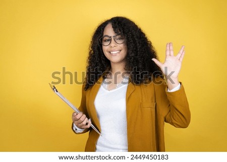 African american business woman with paperwork in hands over yellow background doing star trek freak symbol