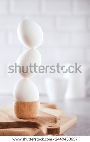 Three white eggs balancing on top of each other. A fun, creative modern motif. Bright color mood. Kitchen scene with egg cups.