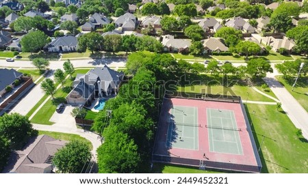 Community tennis courts with chain link fence and players in upscale residential neighborhood with large two-story single-family house, swimming pool, fenced backyard, suburb Dallas, TX, aerial. USA Royalty-Free Stock Photo #2449452321