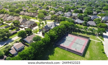 Community tennis courts with chain link fence and players in upscale residential neighborhood with large two-story single-family house, swimming pool, fenced backyard, suburb Dallas, TX, aerial. USA Royalty-Free Stock Photo #2449452323
