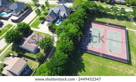 Community tennis courts with chain link fence and players in upscale residential neighborhood with large two-story single-family house, swimming pool, fenced backyard, suburb Dallas, TX, aerial. USA Royalty-Free Stock Photo #2449452347