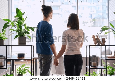 Back view, silhouette of young couple holding hands looking out window