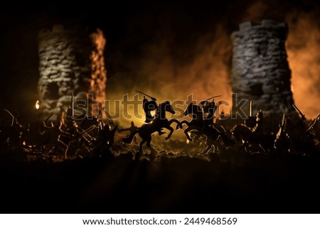 Medieval battle scene with cavalry and infantry. Silhouettes of figures as separate objects, fight between warriors on dark toned foggy background. Night scene. Selective focus Royalty-Free Stock Photo #2449468569