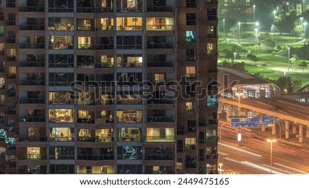 Lights in windows of modern multiple story building in urban setting at night timelapse. Glowing lights in residential skyscraper in Dubai Marina. Traffic on a highway and metro station