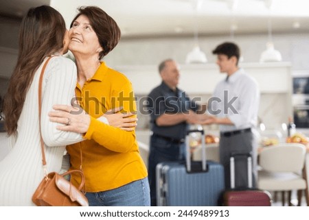 Hospitable friendly elderly woman warmly greeting and kissing daughter-in-law coming for cozy family get-together with set table in background.. Royalty-Free Stock Photo #2449489913