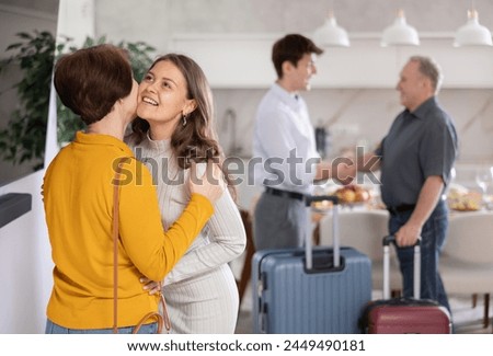Hospitable friendly young woman warmly greeting and kissing mother-in-law coming for cozy family dinner with set table in background.. Royalty-Free Stock Photo #2449490181
