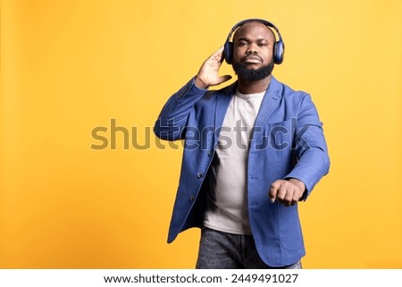 African american man listening to music on wireless stereo headphones during time off. BIPOC audiophile enjoying songs on high fidelity earphones, isolated over studio background Royalty-Free Stock Photo #2449491027