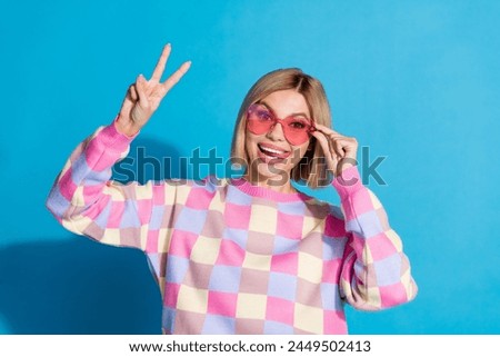Photo portrait of pretty young girl touch sunglass celebrate party show v-sign wear trendy pink outfit isolated on blue color background