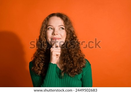 Photo of happy dreamy lady dressed green shirt hand chin looking emtpy space isolated orange color background