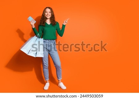 Photo of funky pretty lady dressed green shirt holding shoppers writing device pointing emtpy space isolated orange color background