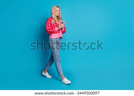 Full size photo of smart person dressed knitwear jumper jeans look at smartphone walk to empty space isolated on blue color background