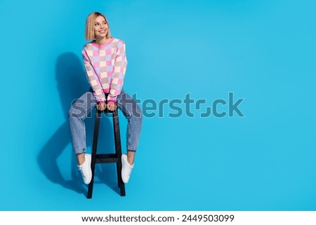Full length photo of pleasant girl wear checkered pullover sit on bar chair look at logo empty space isolated on blue color background