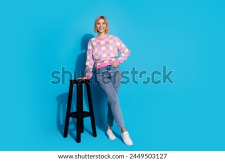 Full length photo of lovely girl wear checkered pullover pants lean on bar chair hold palm in pocket isolated on blue color background