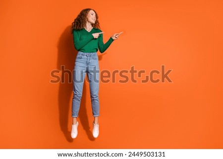 Full length photo of cute dreamy lady dressed green shirt jumping high showing two fingers emtpy space isolated orange color background