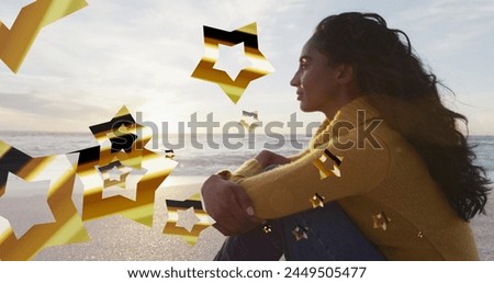 Image of stars over biracial woman at beach. Christmas, celebration and digital interface concept digitally generated image.