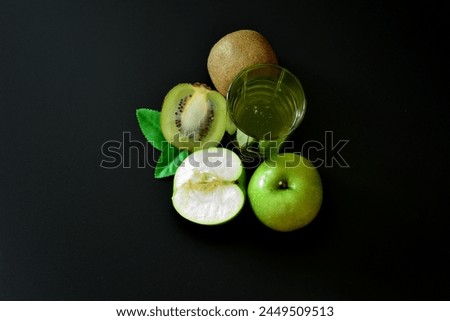 A glass of a mixture of fruit juices on a black background, next to pieces of a ripe kiwi fruit and half a green apple. Close-up.