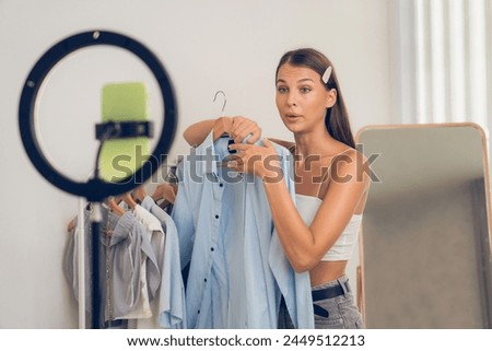 Young woman making fashion video content for social media. Blogger smiles to camera using selfie stick and light ring while making persuasive online clothing sell to audience or followers. Unveiling Royalty-Free Stock Photo #2449512213