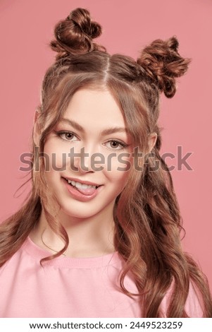Glamorous teenage style. Attractive teenage girl with cute hair bumps on her head and wavy hair, wearing a pink sweatshirt, posing against a pink background.
