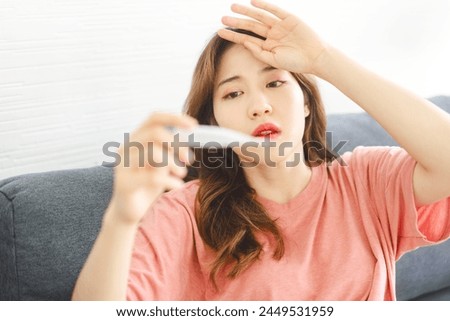 Asian woman got sick using thermometer for checking fever.
People unhealthy from influenza pandemic. Sitting at home sofa. Royalty-Free Stock Photo #2449531959
