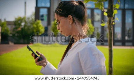 Caucasian woman businesswoman student business lady girl walk on street with green lawn using mobile phone check email browsing social network make order online store on smartphone outdoors side view Royalty-Free Stock Photo #2449534945
