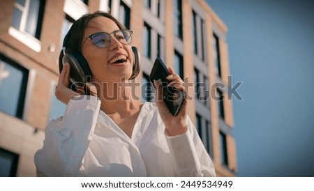 Happy asian woman businesswoman business lady female student listening music sing in headphones using mobile phone outdoors near office building joyful girl listen enjoy song singing moving dancing Royalty-Free Stock Photo #2449534949