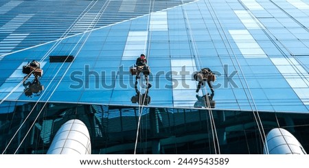 Angle shot group of high rise glass window cleaners climbing on access rope cleaning high rise office building  Royalty-Free Stock Photo #2449543589