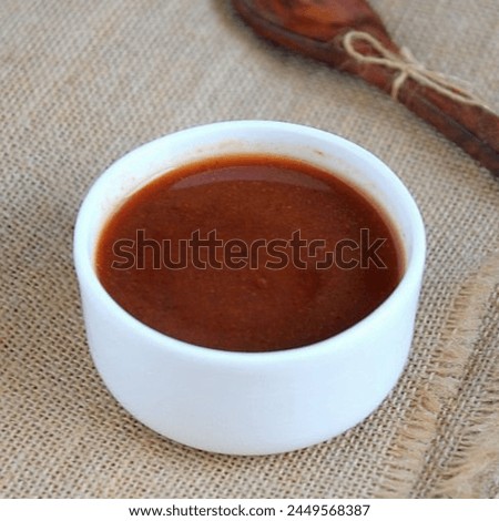 It's a picture of some kind of brown sauce placed inside a white bowl.   Isolated on a rug sheet background with wooden spoon near it.
