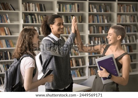 Three happy diverse students met in college library to work together on homework, do joint project, giving high five, greeting each other, enjoy communication. Friendship, highschool, education, team Royalty-Free Stock Photo #2449569171