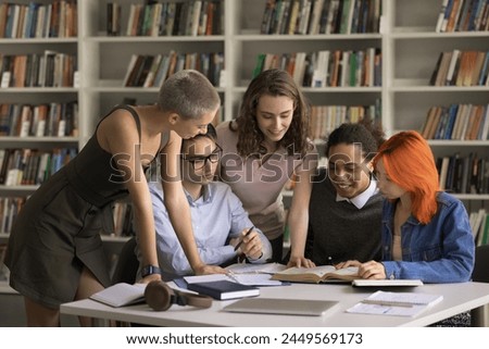 Group of students leaned at desk full of textbook and study materials, discuss joint task, share opinion, learn subject, work on essay, think of solution gathered in university of high-school library Royalty-Free Stock Photo #2449569173