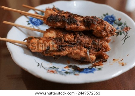 Several skewers of chicken meat in a white plate on a wooden table, traditional meal, Indonesian food, stock photo.