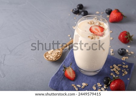 Tasty yogurt in glass, oats and berries on grey table, space for text